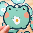 Load image into Gallery viewer, Cute Frog w/ Fried Egg Vinyl Sticker by Fat Rabbit Farm